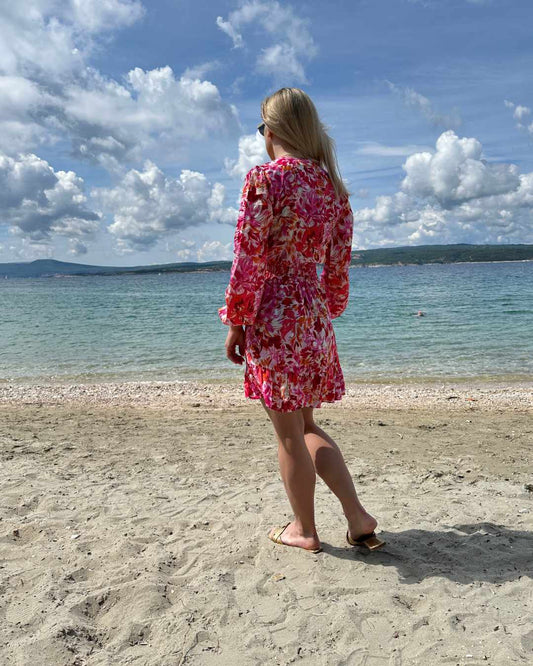 Model ist 160 cm und trägt das kurze Mini Damenkleid mit Blumenmuster. Das Langarm Mini-Klied ist mit V-Ausschnitt. Ein Romantisches-Sommerkleid aus 100 % Viskose und Einheitsgröße XS/M, mit einem Gummiband in der Taille. Hintergrund ist ein Meer der kroatischen Küste der Adria. Nella Fashion Shop