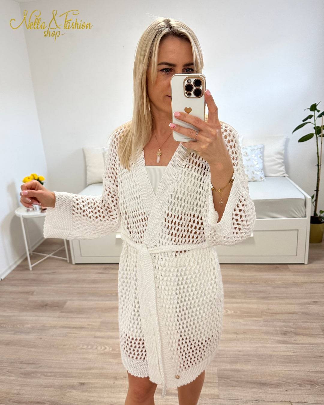 Model präsentiert ein weißes Langarm Cardigan, Einheitsgröße XS bis XL, Wickel mit Taillenbund, perfektes Strandkleid Knielänge, mit Lochmuster. Aus einer Mischung von 50 % Baumwolle und 50 % Acryl. Hintergrund Weiß. Nella Fashion Shop