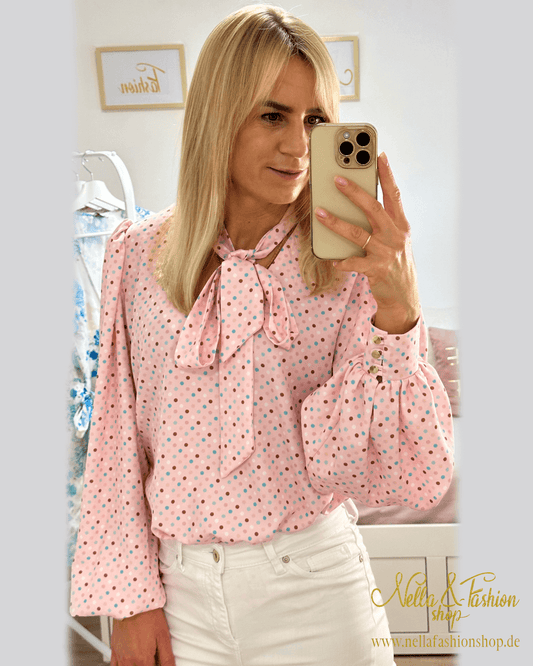 Model präsentiert Damen Hemd mit V-Ausschnitt in Rosa zuzüglich bunt gepunktetes Muster. Das Hemd ist Langarm mit Schleife am Hals, somit kann eine Krawatte gemacht werden. Hemd ist aus 70% Viskose / 30% Polyester. Jetzt bei Nella & Fashion Shop Deutschland