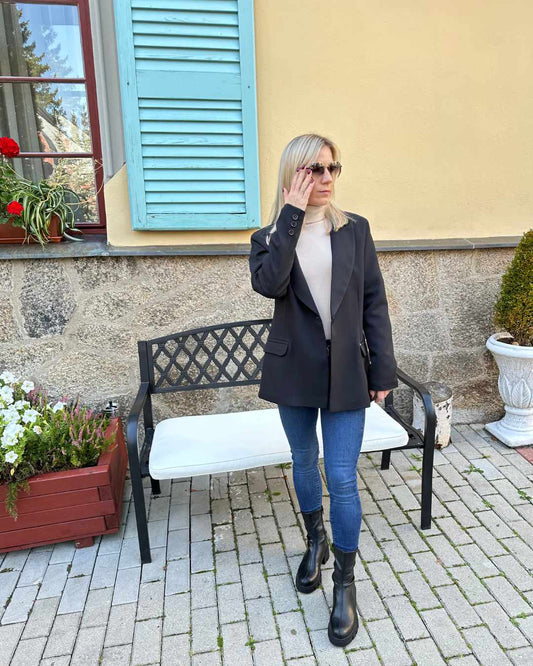 Dieses Model ist 160 cm groß und trägt den klassischen Damen Oversized-Blazer lang, mit einem Knopf, Seitentaschen und geradem Schnitt in der Größe 38, überlangen Ärmel und Schulterposter in Farbe Schwarz. Perfekter für Herbst oder Winter, mit Boots, Rollkragenpullover oder zu einem Kleid.