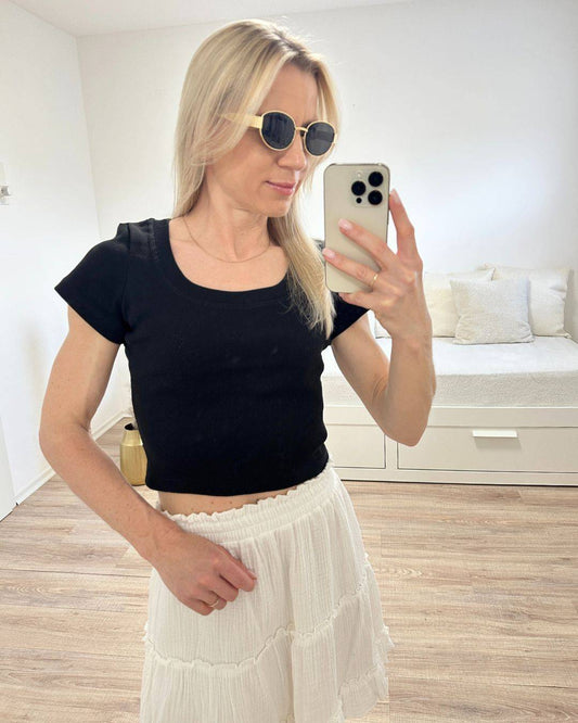 Model trägt das Schwarze Damen Crop Top in Einheitsgröße XS bis M aus 95 % Baumwolle / 5 % Elasthan zusammen mit unseren Weißen Minirock auf ein Weißenhintergrund, Accessoires: Handy, Brille, Nella Fashion Shop Deutschland