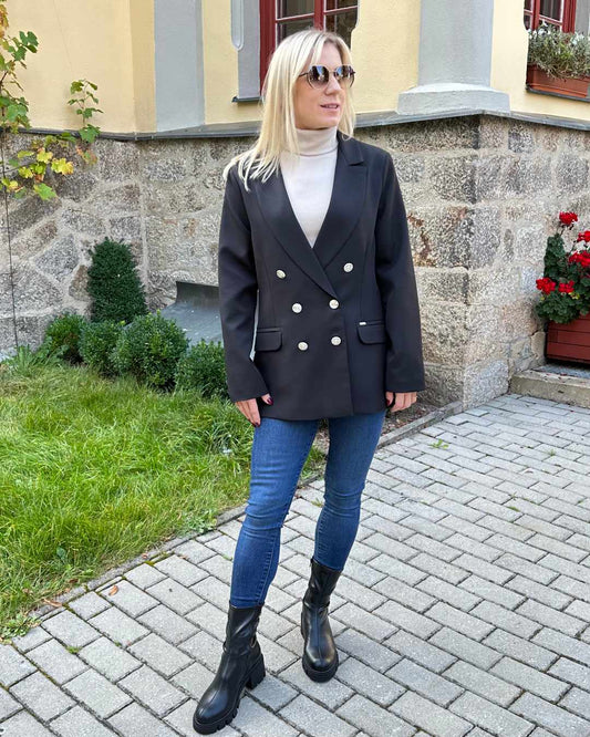 Model ist 160 cm groß und trägt ein Doppelreihiger taillierter schwarzer Damen-Blazer lang, mit Schulterposter, regulärem Schnitt und langen Ärmel in der Größe M. Aus Mischung 60 % Polyester / 35 % Viskose / 5 % Elastan. Der Blazer fällt zu groß aus. Vorne mit 6 goldenen Knöpfen in der mitte. Perfekter für Herbst oder Winter, mit Boots, Rollkragenpullover oder zu einem Kleid. Hintergrund ist ein Hotel in Tschechien. Nella Fashion Shop