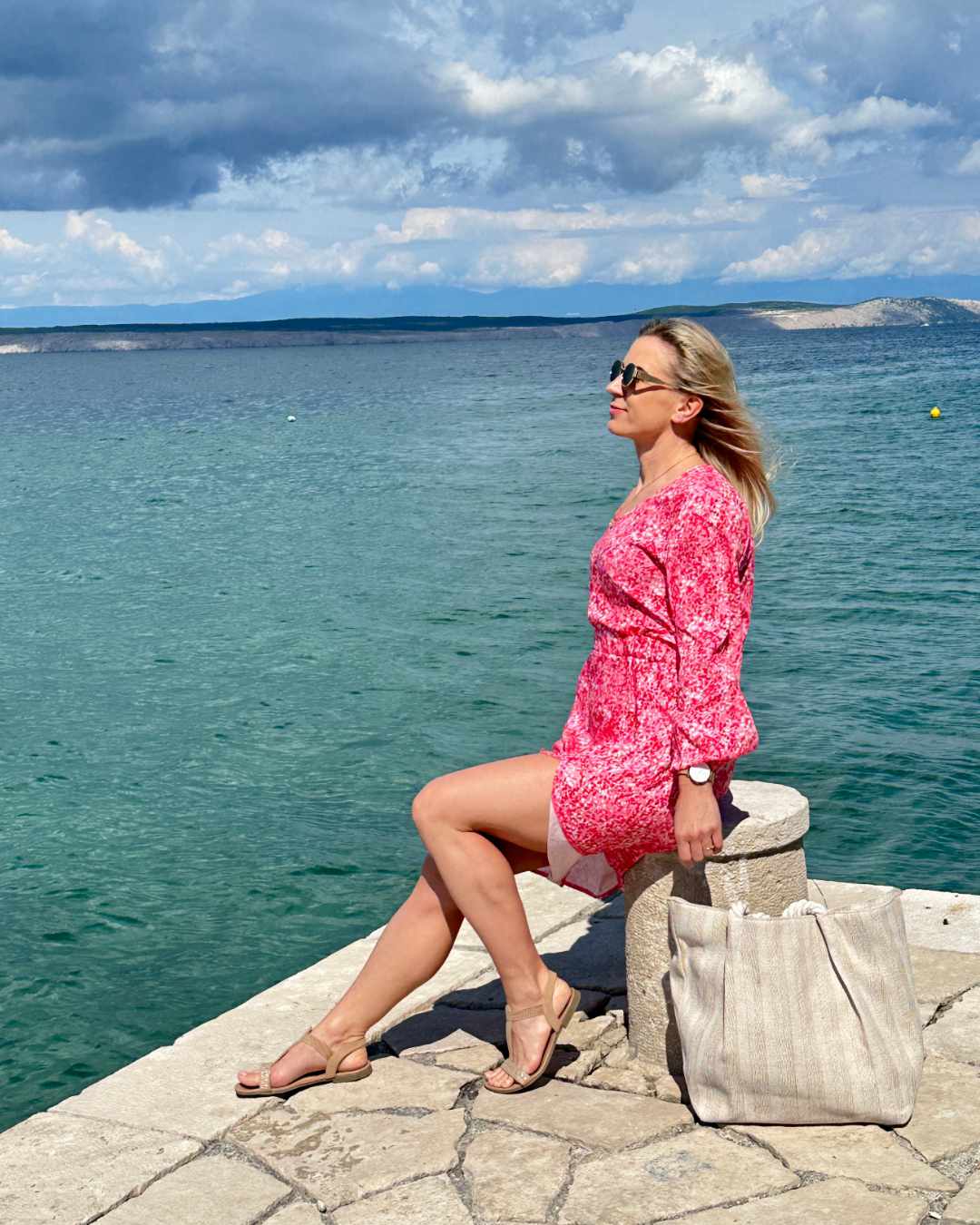 Model ist 160 cm groß und präsentiert von Hinten das S/M Knöchellanges elegantes Midi Langarm-Kleid in Rosa mit Weißen Punktenmuster, mit V-Ausschnitt, Seitenschlitz und elastischen Gummibündchen an den Armen sowie in der Teile, aus 60 % Viskose, 35 % Polyester, 5 % Elasthan, erhältlich in Größe S/M und L/XL, alles auf ein Meer Hintergrund, perfekt für Urlaub, Meer, Unterwegs, online kaufen bei Nella Fashion Shop