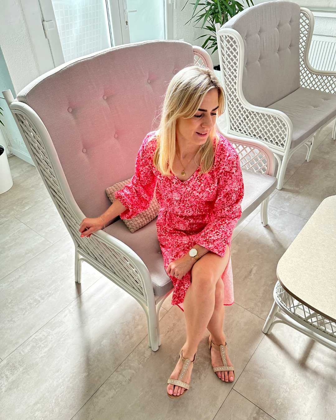 Model ist 160 cm groß und trägt das S/M Knöchellanges elegantes Midi Langarm-Kleid in Rosa mit Weißen Punktenmuster, mit V-Ausschnitt, Seitenschlitz und elastischen Gummibündchen an den Armen sowie in der Teile, aus 60 % Viskose, 35 % Polyester, 5 % Elasthan, erhältlich in Größe S/M und L/XL, Sie sitzt auf einen Sessel in Büro Hintergrund, perfekt für Urlaub, Meer, Unterwegs, bei Nella Fashion Shop Deutschland