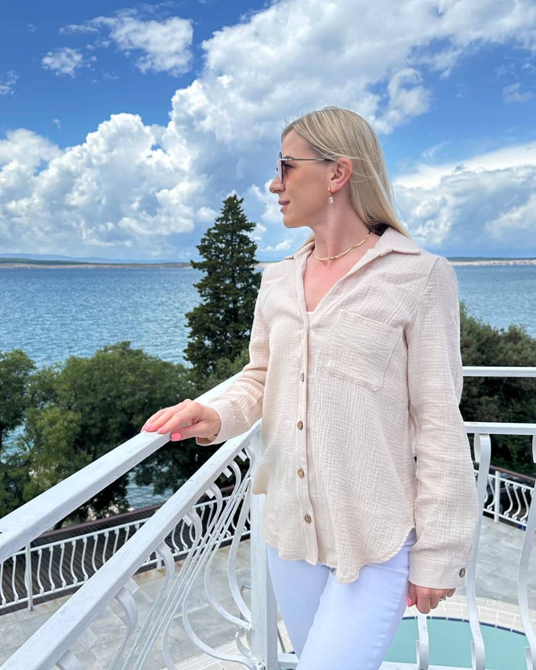 Model präsentiert den Langarm Damen Musselin Hemd aus 100 % Baumwolle in Beige. Leicht, locker und elegant Sommerhemd für Damen aus Musselin. In Oversized-Schnitt und Brusttasche, sowie Seiten Schlitz. Erhältlich in XS/S und M/L, Schwarz und Beige bei Nella Fashion Shop. Hintergrund ist ein Meer der kroatischen Küste der Adria.