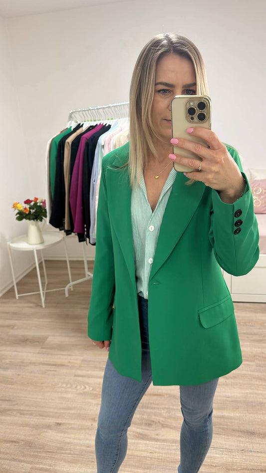 Model ist 160 cm groß und trägt ein Klassischer Damen Oversized-Blazer lang, mit einem Knopf, Seitentaschen und geradem Schnitt in der Größe 36. Farbe Grün, überlangen Ärmel und Schulterposter. Kombiniert mit Hosen und Hemd ein perfektes Outfit für Herbst oder Winter, mit Boots, Rollkragenpullover oder zu einem Kleid. Hintergrund ist Weiß. Nella Fashion Shop