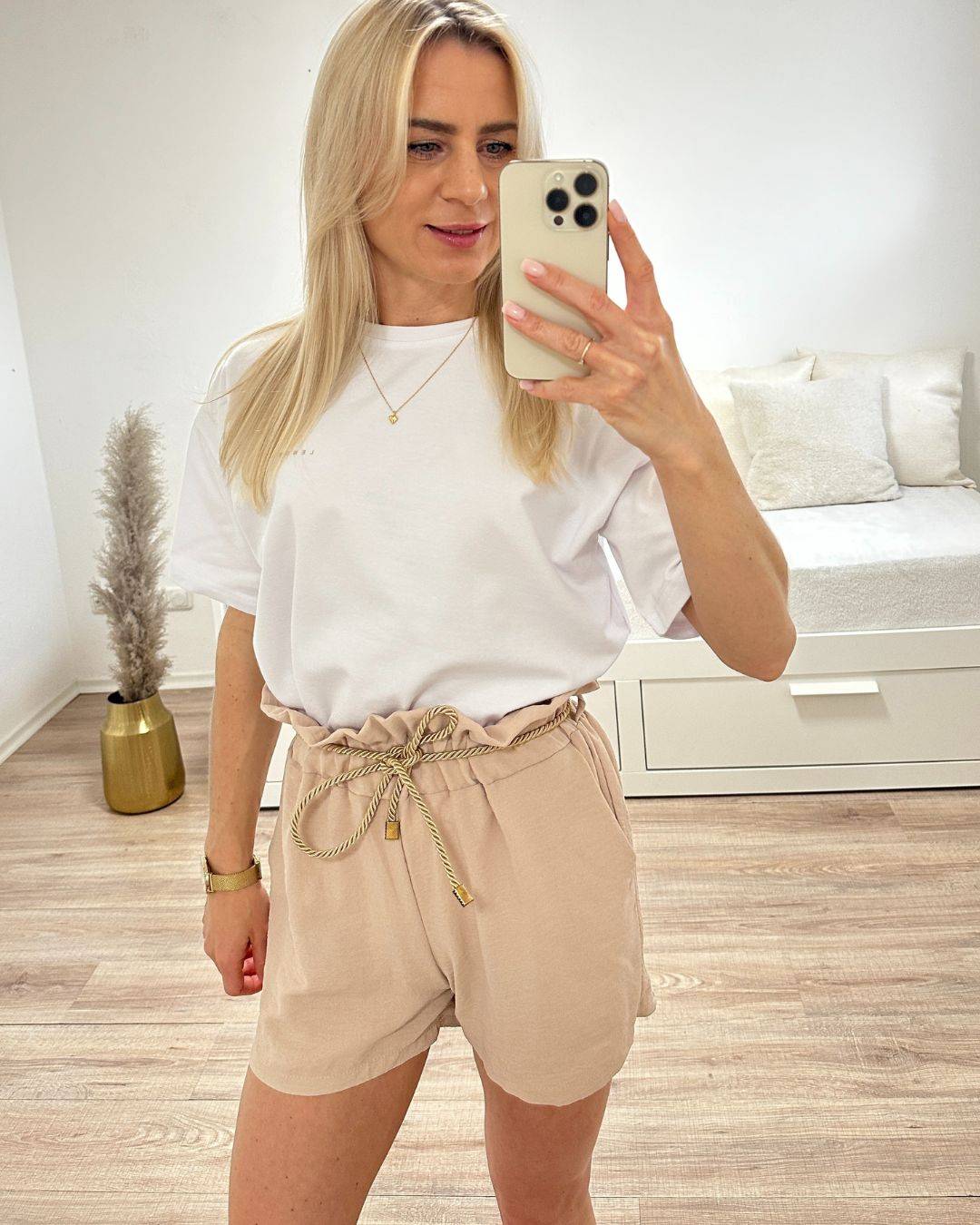 Model trägt das Weiße Rundhals T-Shirt in Einheitsgröße XS bis L aus 95 % Baumwolle / 5 % Elastan dazu unsere kurze Hose in Beige aus ein Weißenhintergrund, Accessoires: Handy, Halskette, Armbanduhr online kaufen Nella Fashion Shop
