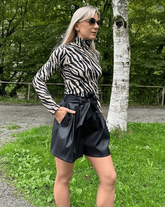 Model präsentiert den Damen Herbst Outfit Kunstleder Shorts Schwarz in Größe XS mit Damen Rollkragenpullover Langarm in Zebramuster Größe S, aus 95 % Baumwolle / 5 % Elasthan. Nella Fashion Shop. Hintergrund Spazieren in Park.