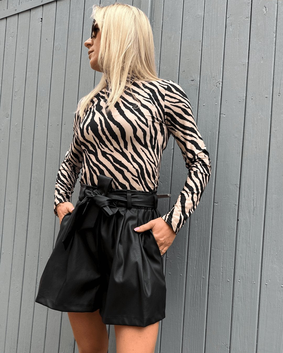 Model ist 160 cm groß präsentiert Herbst Outfit,  Damen Rollkragenpullover mit Zebramuster dazu Kunstlederhosen mit Schleife in Schwarz auf ein Weißenhintergrund,  Foto für Rollkragenpullover Kollektion bei Nella Fashion Shop Deutschland 