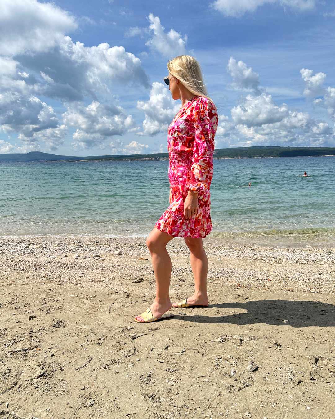 Model ist 160 cm und trägt das kurze Mini Damenkleid mit Blumenmuster. Das Langarm Mini-Klied ist mit V-Ausschnitt. Ein Romantisches-Sommerkleid aus 100 % Viskose und Einheitsgröße XS/M, mit einem Gummiband in der Taille. Hintergrund ist ein Meer der kroatischen Küste der Adria. Nella Fashion Shop