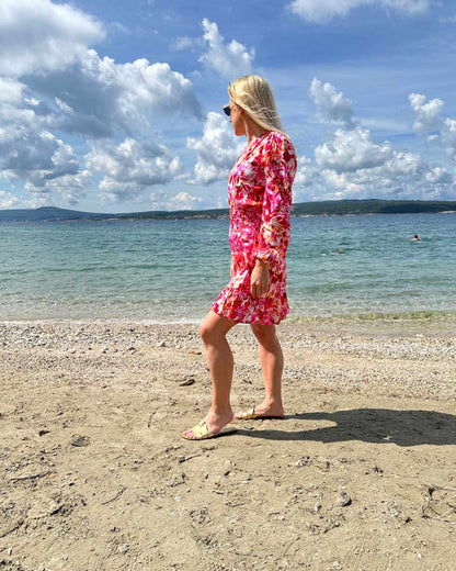 Model ist 160 cm und trägt das kurze Mini Damenkleid mit Blumenmuster. Das Langarm Mini-Klied ist mit V-Ausschnitt. Ein Romantisches-Sommerkleid aus 100 % Viskose und Einheitsgröße XS/M, mit einem Gummiband in der Taille. Hintergrund ist ein Meer der kroatischen Küste der Adria. Nella Fashion Shop