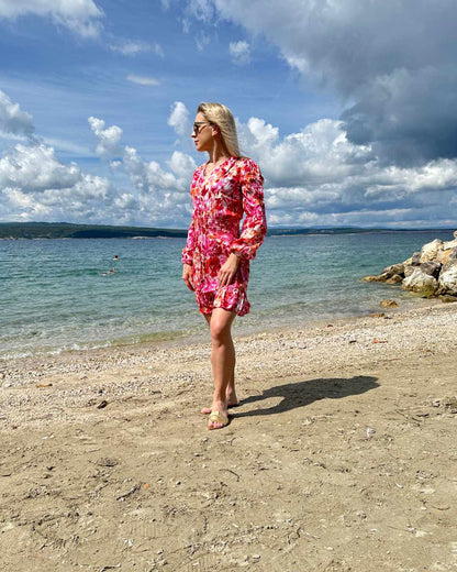 Model ist 160 cm und trägt das kurze Mini Damenkleid mit Blumenmuster. Das Langarm Mini-Klied ist mit V-Ausschnitt. Ein Romantisches-Sommerkleid aus 100 % Viskose und Einheitsgröße XS/M, mit einem Gummiband in der Taille. Hintergrund ist ein Meer der kroatischen Küste der Adria. Nella Fashion Shop