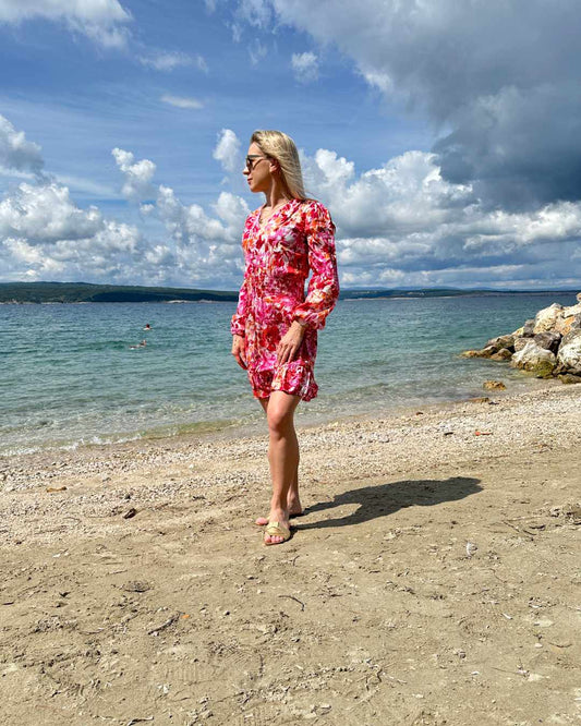 Model ist 160 cm und trägt das kurze Mini Damenkleid mit Blumenmuster. Das Langarm Mini-Klied ist mit V-Ausschnitt. Ein Romantisches-Sommerkleid aus 100 % Viskose und Einheitsgröße XS/M, mit einem Gummiband in der Taille. Hintergrund ist ein Meer der kroatischen Küste der Adria. Nella Fashion Shop