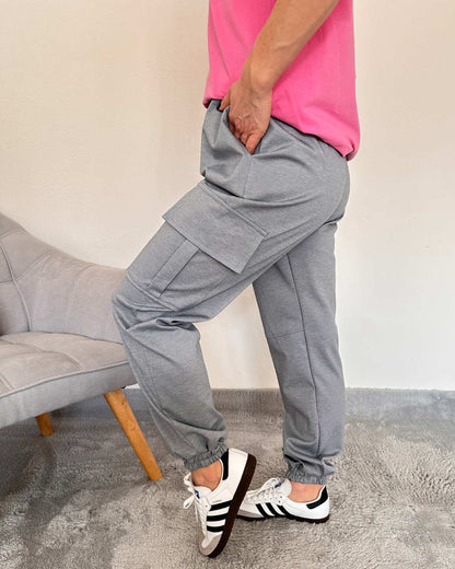 Model hat die Damen Army Cargopants in Trendfarbe Grau aus Materialzusammensetzung
65 % Baumwolle / 35 % Polyester.  In der Einheitsgröße (von XS bis L). Mit einem Gummizug am Knöchel und an der Teile. Große Seitentaschen mit Funktionalität und Style. Weißer Hintergrund. Jetzt bei Nella & Fashion Shop