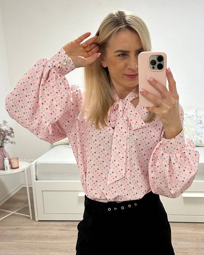 Model hat das Langarm-Hemd in Rosa zuzüglich mit bunt gepunktetes Muster. Das Hemd ist Langarm mit Schleife am Hals, somit kann eine Krawatte gemacht werden. V-Ausschnitt und weiten Armen. Alles auf ein Weißenhintergrund, Nella Fashion Online Shop   