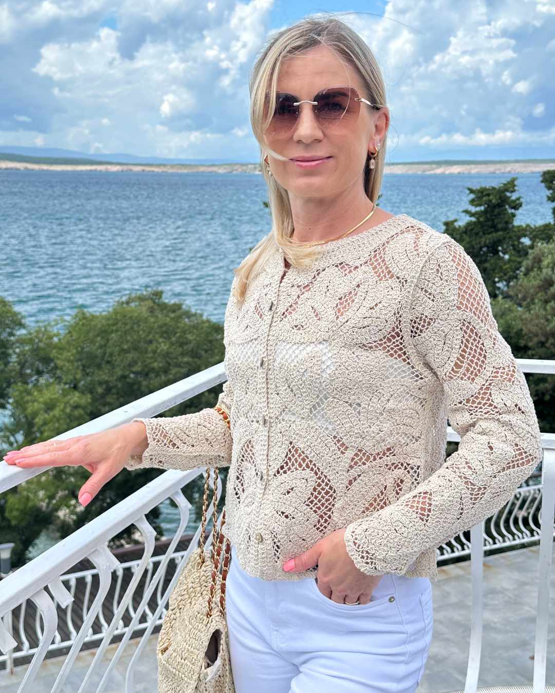 Model präsentiert von vorne den Damen Boho Rundhals Strickpullover mit der offenen Strickart kleine Löcher. Hintergrund ist ein Meer der kroatischen Küste der Adria. Erhältlich bei Nella Fashion Shop in S/M oder M/L 