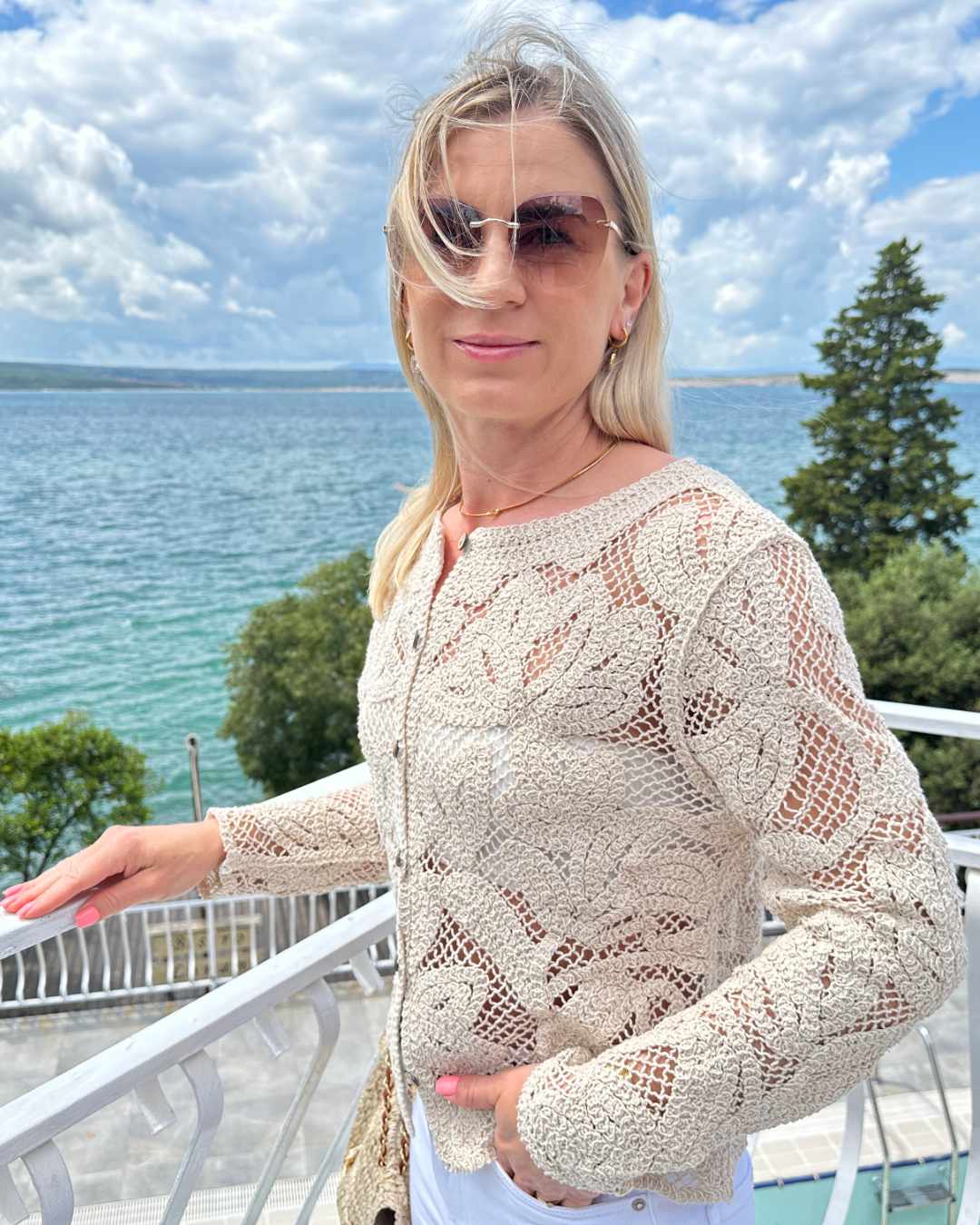 Model präsentiert Damen Boho Rundhals Strickpullover aus 100 % Baumwolle in Beige und Größe S/M oder M/L mit Holzknöpfen Verschluss jetzt bei Nella Fashion Shop Hintergrund ist ein Meer der kroatischen Küste der Adria.
