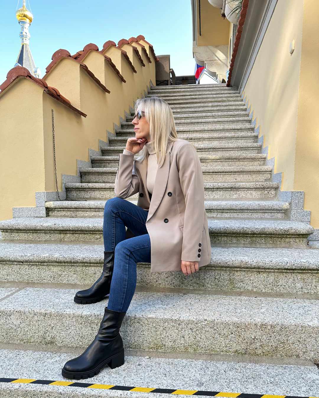 Model präsentiert ein Damen Doppelreihiger Oversized-Blazer lang mit Puffärmeln in Beige, mit Schwarzen Knöpfen verziert in der Mitte und am Manschetten. Asu 60 % Polyester / 35 % Viskose / 5 % Elastan Mischung. Jetzt bei Nella Fashion Shop in der Größe 36 und  38 kaufen. Hintergrund Hotel Treppen. 