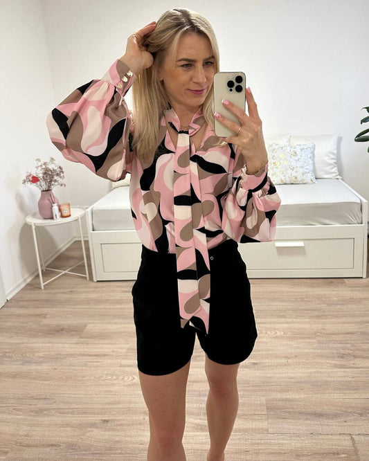 Model präsentiert Damen-Hemd mit V-Ausschnitt in Abstract zuzüglich Rosa-Weiß-Schwarz und Braunen Farben Muster. Das Hemd ist Langarm mit Schleife am Hals, somit kann eine Krawatte gemacht werden. Hemd ist aus 70% Viskose / 30% Polyester. Jetzt bei Nella & Fashion Shop Deutschland