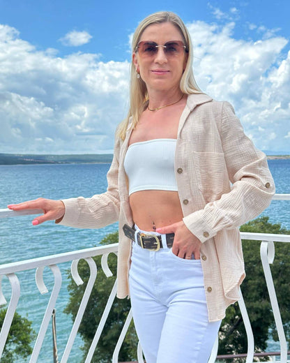 Model präsentiert den Langarm Damen Musselin Hemd aus 100 % Baumwolle in Beige. Leicht, locker und elegant Sommerhemd für Damen aus Musselin. In Oversized-Schnitt und Brusttasche, sowie Seiten Schlitz. Erhältlich in XS/S und M/L, Schwarz und Beige bei Nella Fashion Shop. Hintergrund ist ein Meer der kroatischen Küste der Adria. 