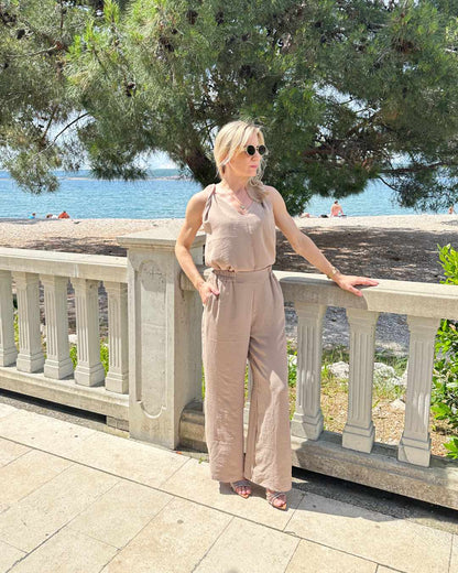 Model präsentiert das Sommeroutfit Laura Damen Tank Top mit V-Ausschnitt plus Hosen mit weiten Beinen und hohem Bund zzgl. ein Gummi in der Taille in Beige Größe M/L. Alles auf eine kroatische Küste der Adria Hintergrund. Jetzt bei Nella Fashion Shop kaufen