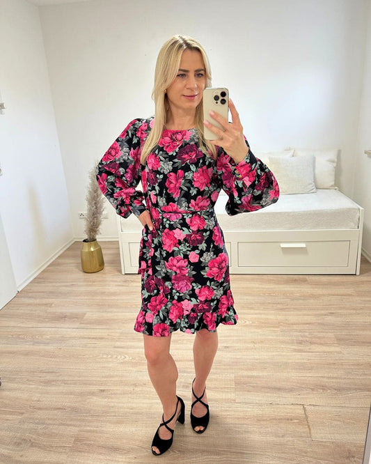 Model hat das Damen-Wickelkleid MARBELLLA in der Größe S an. Die Rosen Blumen Muster Mini Kleid, ist Rundhalsausschnitt und Langarm. Erhältlich in Größen S, M oder L bei Nella Fashion Shop Deutschland und aus 70 % Viskose und 30 % Polyester. Foto auf weißem Hintergrund. 