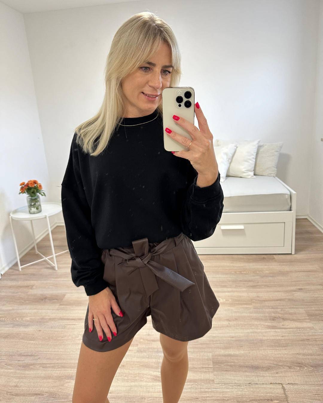 Model ist 160 cm und trägt unsere Damen Kunstleder Shorts mit hohem Bund in Schokoladenfarben Größe 34 aus 95 % Polyester / 5 % Elastan mit einer Schleife/Gürtel und Seitentaschen, kombiniert mit Kurze-Oversized-Sweatshirt XXL Forma, perfektes lässiges Outfit für Frauen, auf Weißen Hintergrund, Nella Fashion Shop  