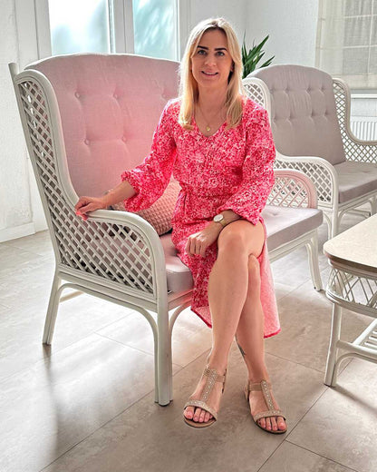 Model ist 160 cm groß und trägt das S/M Knöchellanges elegantes Midi Langarm-Kleid in Rosa mit Weißen Punktenmuster, mit V-Ausschnitt, Seitenschlitz und elastischen Gummibündchen an den Armen sowie in der Teile, aus 60 % Viskose, 35 % Polyester, 5 % Elasthan, erhältlich in Größe S/M und L/XL, Sie sitzt auf einen Sessel in Büro Hintergrund, perfekt für Urlaub, Meer, Unterwegs, bei Nella Fashion Shop Deutschland
