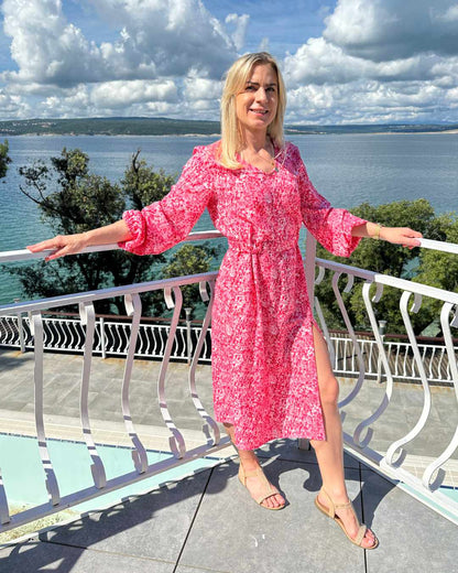 Model ist 160 cm groß und trägt das S/M Knöchellanges elegantes Midi Langarm-Kleid in Rosa mit Weißen Punktenmuster, mit V-Ausschnitt, Seitenschlitz und elastischen Gummibündchen an den Armen sowie in der Teile, aus 60 % Viskose, 35 % Polyester, 5 % Elasthan, erhältlich in Größe S/M und L/XL, alles auf ein Meer Hintergrund, perfekt für Urlaub, Meer, Unterwegs, online kaufen bei Nella Fashion Shop