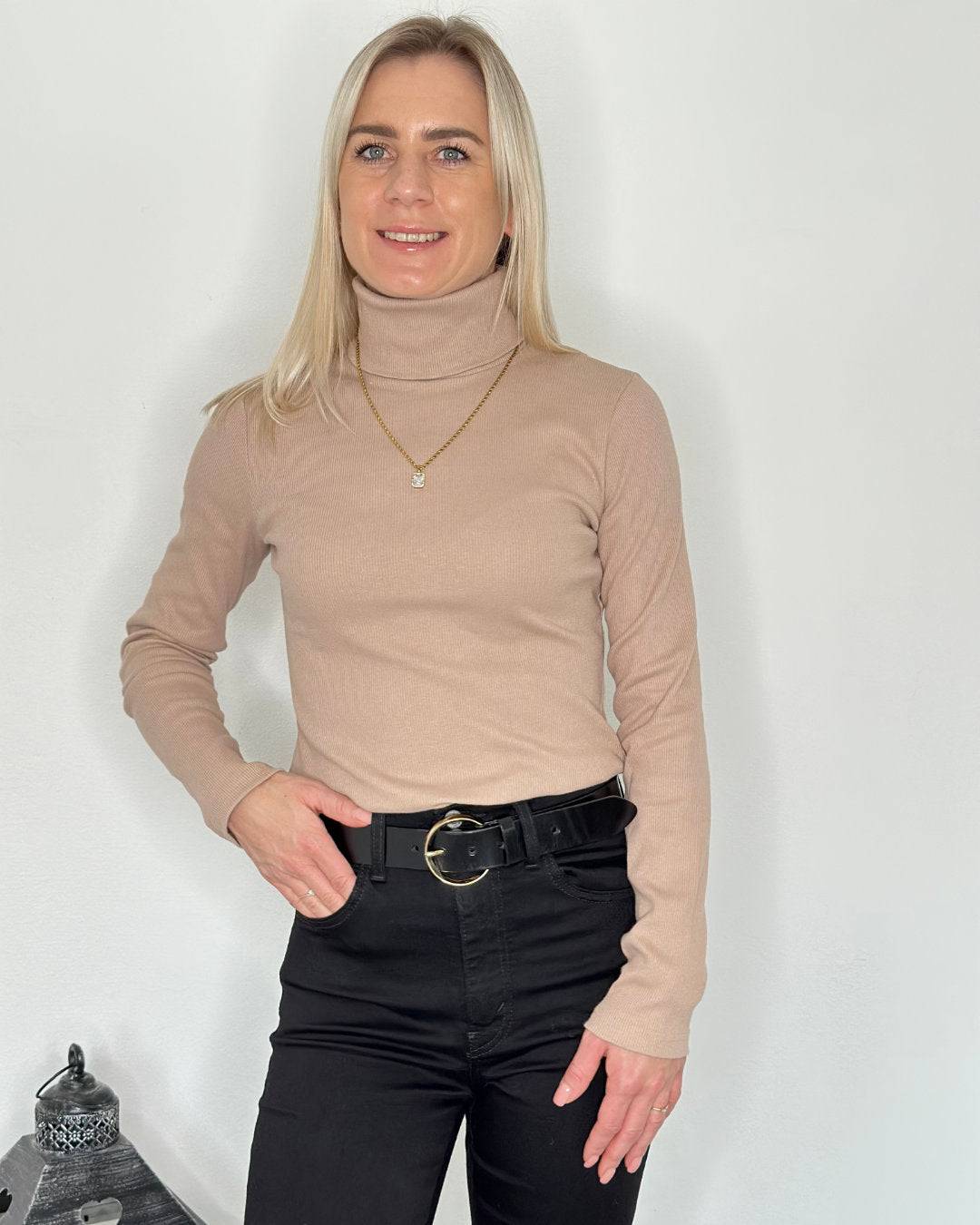 Model hat den Damen Gerippter Rollkragenpullover, Dunkel beige Langarm Größe M aus 95 % Baumwolle. Passt Perfekt. Hintergrund Weiße Wand. Nella Fashion Shop  