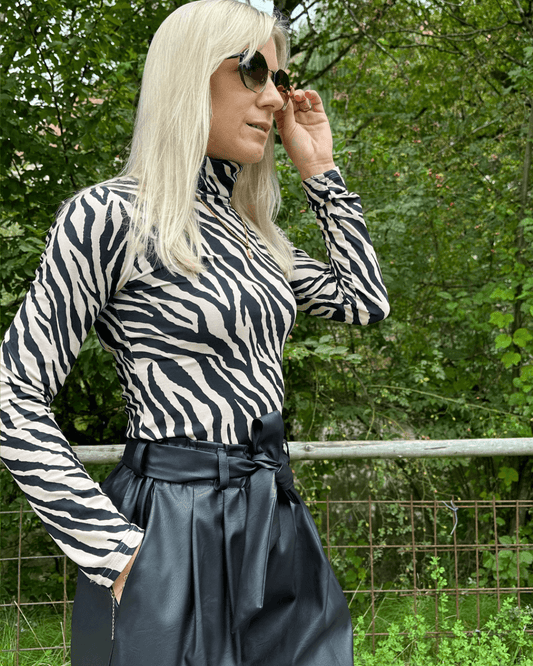 Model hat Damen Herbst Outfit Kunstleder Shorts Schwarz in Größe XS mit Damen Rollkragenpullover Langarm in Zebramuster Größe S. Jetzt bei Nella Fashion Shop nur Größe L. Hintergrund Park.