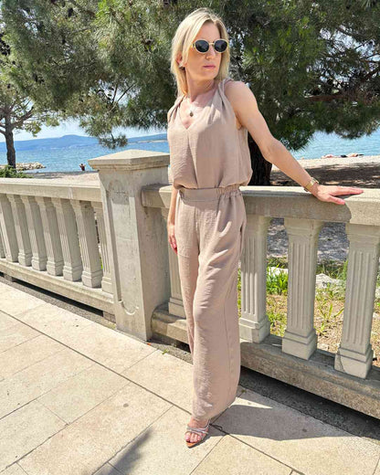 Model trägt das Sommeroutfit Laura für Damen Tank Top mit V-Ausschnitt plus Hosen mit weiten Beinen und hohem Bund zzgl. ein Gummi in der Taille in Beige Größe M/L. Material 97 % Polyester / 3 % Lycra. Alles auf eine kroatische Küste der Adria Hintergrund. Jetzt bei Nella Fashion Shop kaufen
