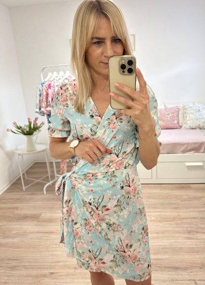 Mini Wickel Sommerkleid für Damen mit Hellblau mit Rosa Blumenmuster in Größe S, M, L, Kurzarm wird von innen mit einer Schleife zusammengebunden und passt sich so jeder Figur perfekt an. Der V-Ausschnitt verleiht dezent die Weiblichkeit. Kleider "NELLA" Inspiration für verschiedene Anlässe wie Taufe, sowie für Sommertage.