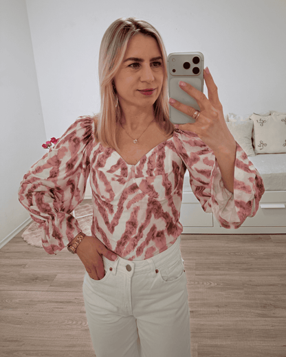 Model trägt die spanische Damenbluse mit Rosa Zebra-Muster in der Größe S. Aus 60 % Polyester / 35 % Viskose / 5 % Elastan Mischung. Getragen als schulterfreien Oberteilen. Spanische Carmen-Bluse ist Langarm, mit einem Gummiband am Arm  angezogen und mit Rüsche beendet, dazu Gummiband an der Schulter und Brustumfang. Hintergrund Weiß. Jetzt bei Nella Fashion Shop Deutschland S und M Größe