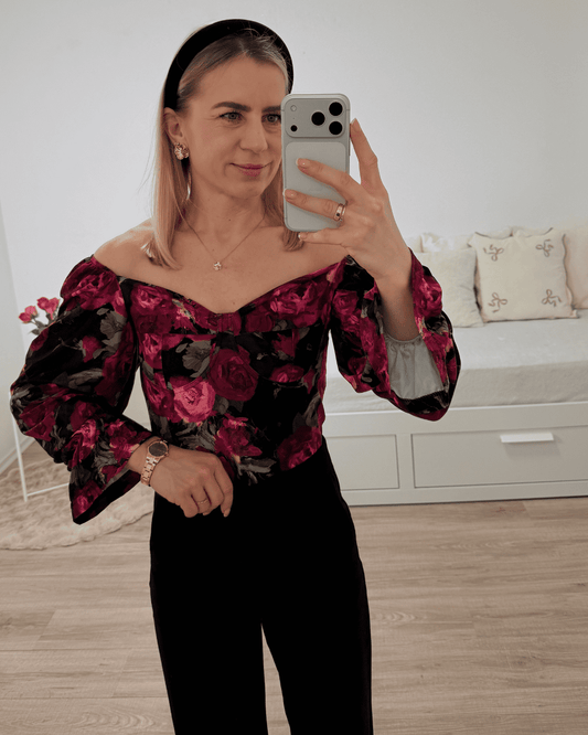 Model trägt die spanische Damenbluse mit roten Rosen-Muster in der Größe S. Aus 60 % Polyester / 35 % Viskose / 5 % Elastan Mischung. Getragen als schulterfreien Oberteilen. Spanische Carmen-Bluse ist Langarm, mit einem Gummiband am Arm  angezogen und mit Rüsche beendet, dazu Gummiband an der Schulter und Brustumfang. Hintergrund Weiß. Jetzt bei Nella Fashion Shop Deutschland S und M Größe