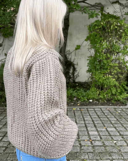 Model präsentiert bei Stehen in Park den Oversized-Strickpullover Rundhals mit Zopfmuster Langarm Einheitsgröße XS/L in Beige aus Materialien 15 % Mohair / 15 % Wolle / 10 % Polyester / 60 % Acryl. Erhältlich bei Nella Fashion Shop in Weiß, Dunkel beige, Schokoladenfarbe. 