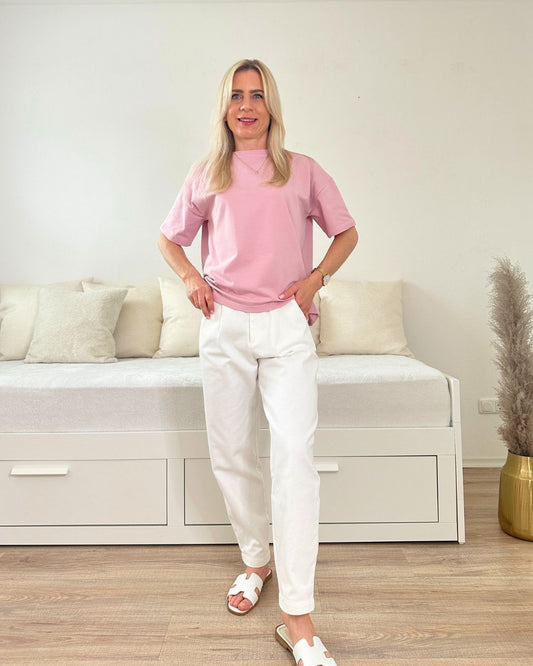 Model trägt das Rosa Rundhals T-Shirt in Einheitsgröße XS bis L aus 95 % Baumwolle / 5 % Elastan dazu unsere Hosen in Ecru aus ein Weißenhintergrund, Accessoires: Latschen, online kaufen Nella Fashion Shop