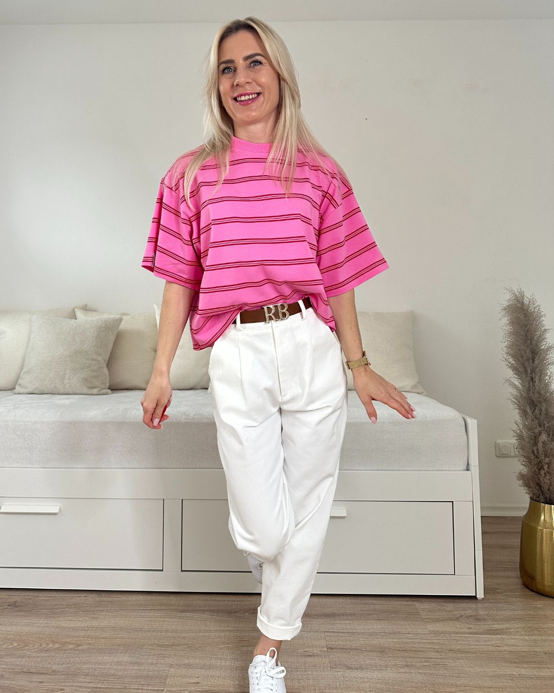 Model trägt das Rosa Damen Oversized T-Shirt in Streifen mit passenden Ecru Hosen auf ein Weißenhintergrund, Accessoires: Gürtel von unserer Tunika, Schuhe, Armbanduhr, Online Nella Fashion Shop