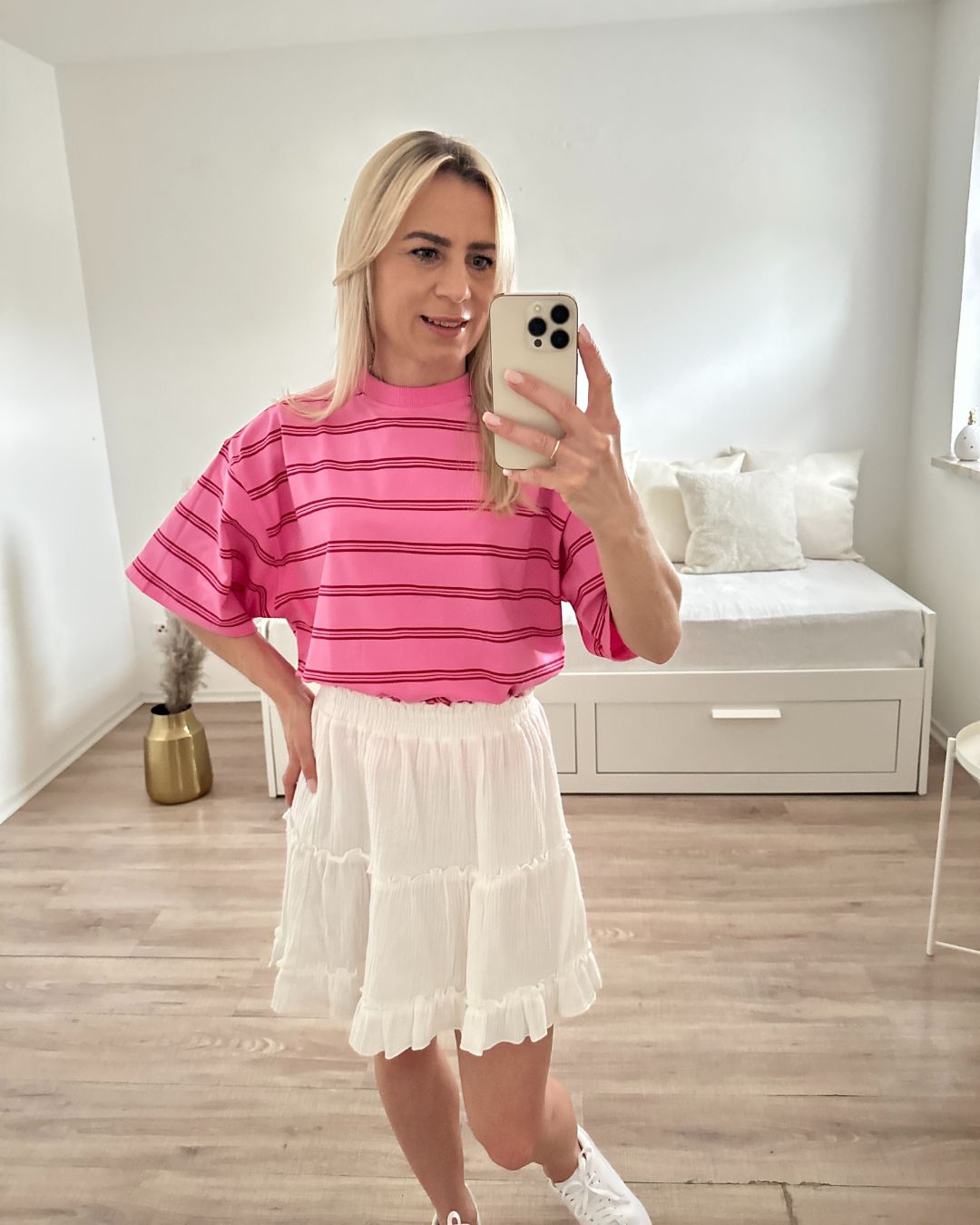 Model trägt das Rosa T-Shirt mit Streifen und breiten Arm aus 95 % Baumwolle, 5 % Elastan, dazu unseres Weißes Minirock aus Baumwolle auf ein Weißenhintergrund, perfekter Sommerlook für unterwegs, Urlaub, Strand, Accessoires: Schuhe, Handy, online Kaufen Nella Fashion Shop  