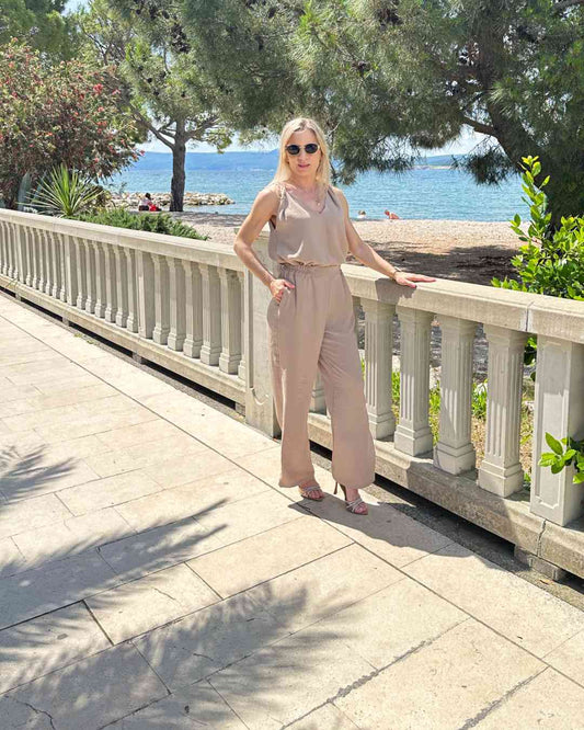 Model ist 160 cm groß und hat das zweiteilige Laura Sommeroutfit für Damen an. Set aus Tank Top mit Tiefen Dekolleté plus Hosen mit weiten Beinen in Beige. Größe M/L fällt zu groß aus! Hosen sind mit einem hohen Bund und Gummiband in der Taille - elastisch. Der Perfekte Elegant und lässig Strand Style für deinen Urlaub. Alles auf eine kroatische Küste der Adria Hintergrund. Nella Fashion Shop