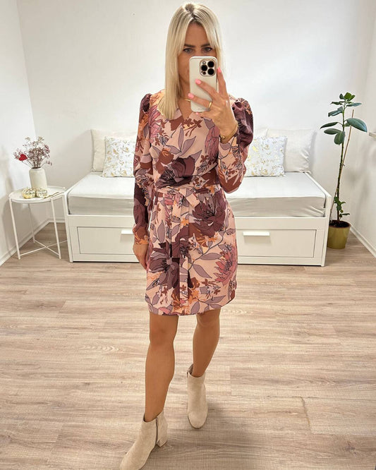 Model ist 160 cm groß und hat das Damen-Wickel-Kleid ALMERIA 1 in Blumen-Muster an. Knielänge, V-Ausschnitt und zusätzlich eine Schleife in Taille zum Binden betonen die Figur. Perfektes Herbst Kleid mit Blumenmuster kann sehr gut mit Damen Boots kombiniert werden. Foto auf einen weißen Hintergrund. Nella Fashion Shop 