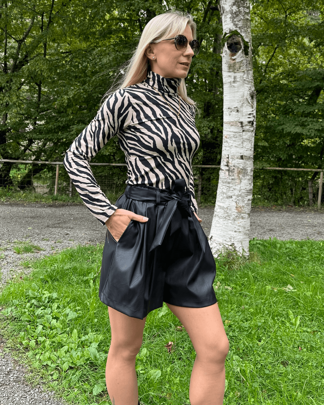 Model präsentiert den Damen Herbst Outfit Kunstleder Shorts Schwarz in Größe XS mit Damen Rollkragenpullover Langarm in Zebramuster Größe S, aus 95 % Baumwolle / 5 % Elasthan. Nella Fashion Shop. Hintergrund Spazieren in Park. 
