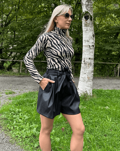 Model präsentiert den Damen Herbst Outfit Kunstleder Shorts Schwarz in Größe XS mit Damen Rollkragenpullover Langarm in Zebramuster Größe S, aus 95 % Baumwolle / 5 % Elasthan. Nella Fashion Shop. Hintergrund Spazieren in Park. 